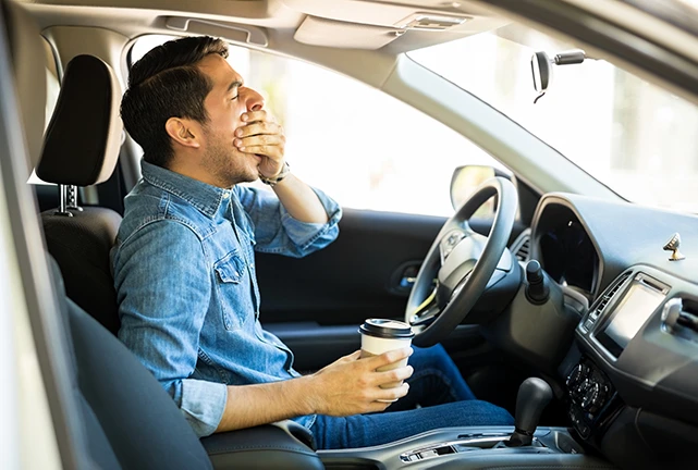 Image of man driving tired with coffee in hand